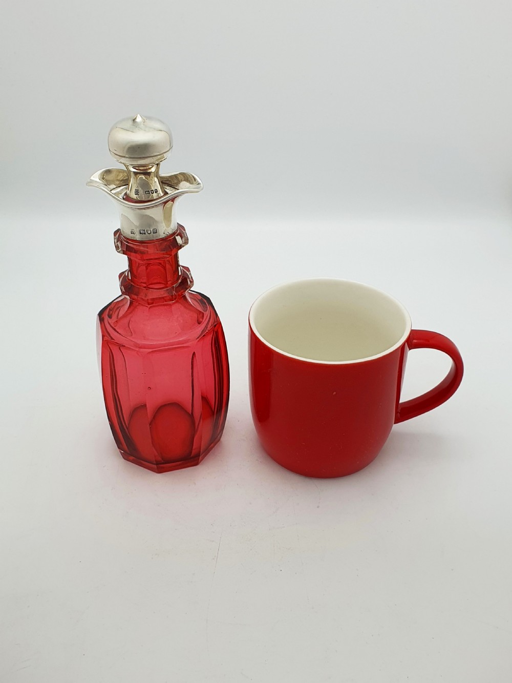 An Edwardian cranberry glass decanter featuring a faceted red body, a hallmarked sterling silver collar with a poured lip, and a matching silver stopper. View VIII