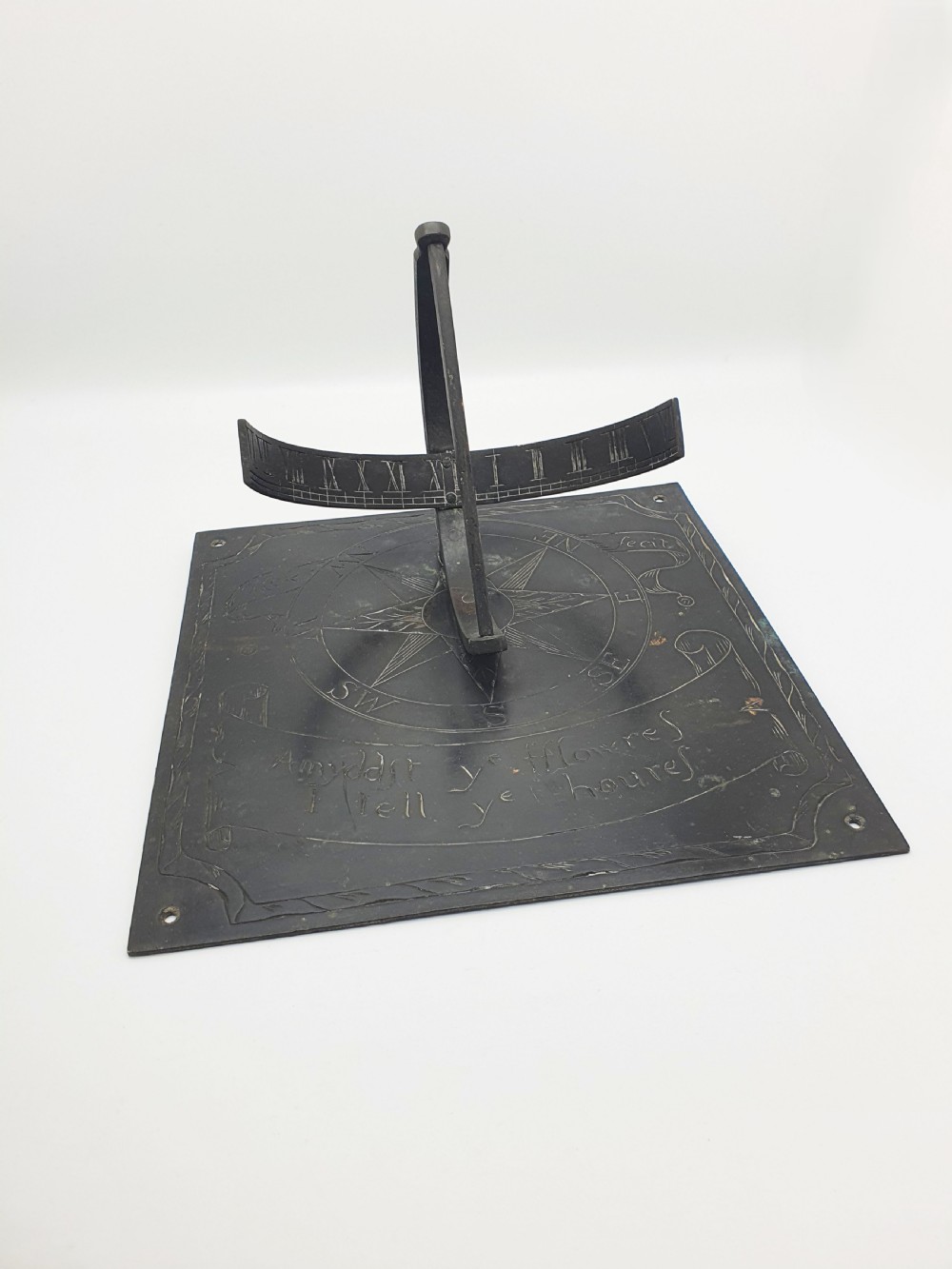 A square dark patinated brass sundial plate featuring engraved compass markings, verse inscription, and a curved armillary gnomon arc.