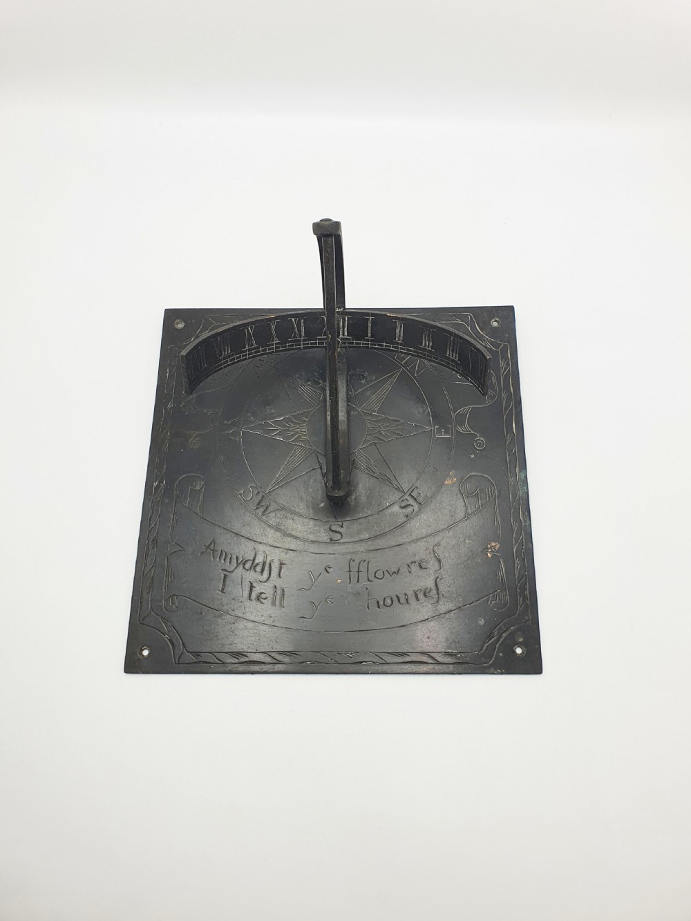 A square dark patinated brass sundial plate featuring engraved compass markings, verse inscription, and a curved armillary gnomon arc. View II