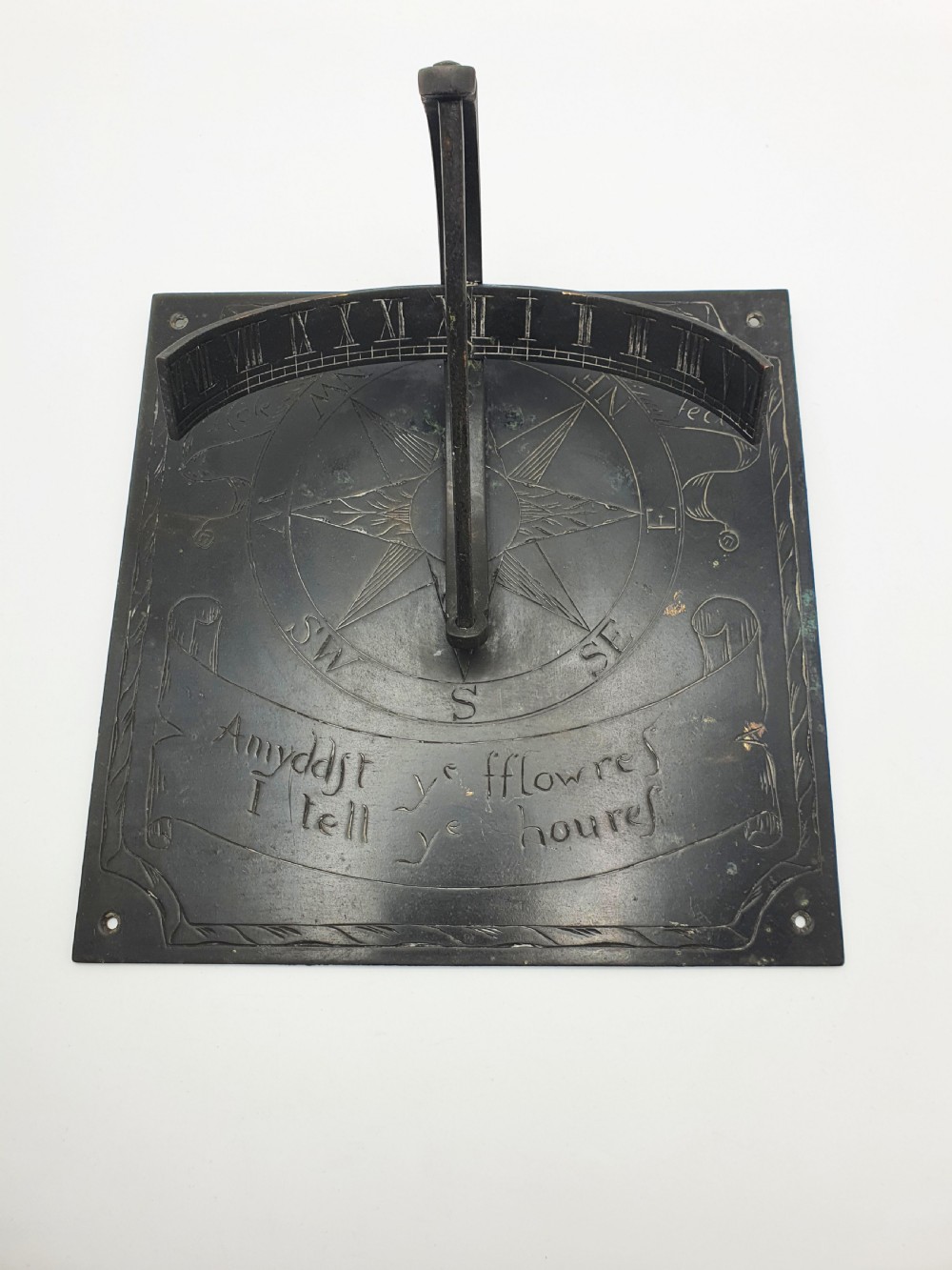 A square dark patinated brass sundial plate featuring engraved compass markings, verse inscription, and a curved armillary gnomon arc. View III