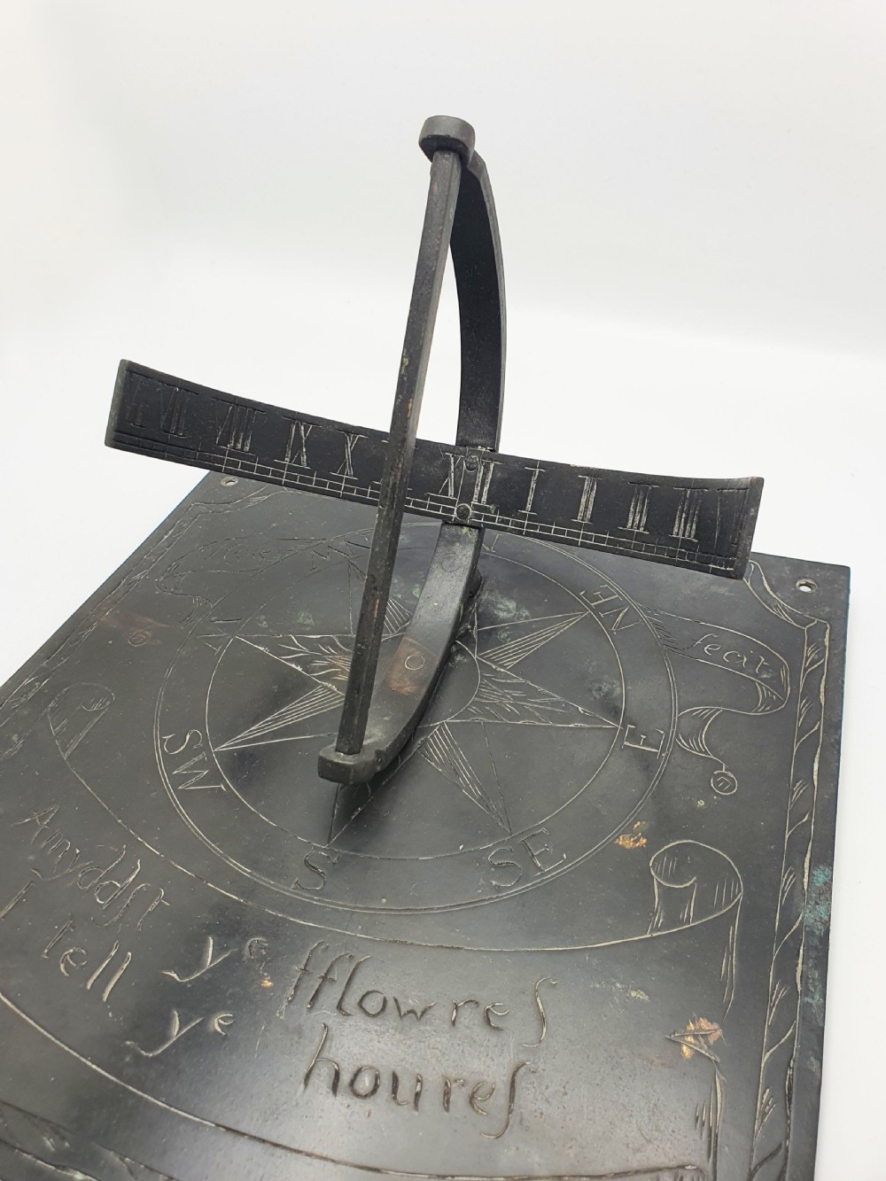 A square dark patinated brass sundial plate featuring engraved compass markings, verse inscription, and a curved armillary gnomon arc. View V