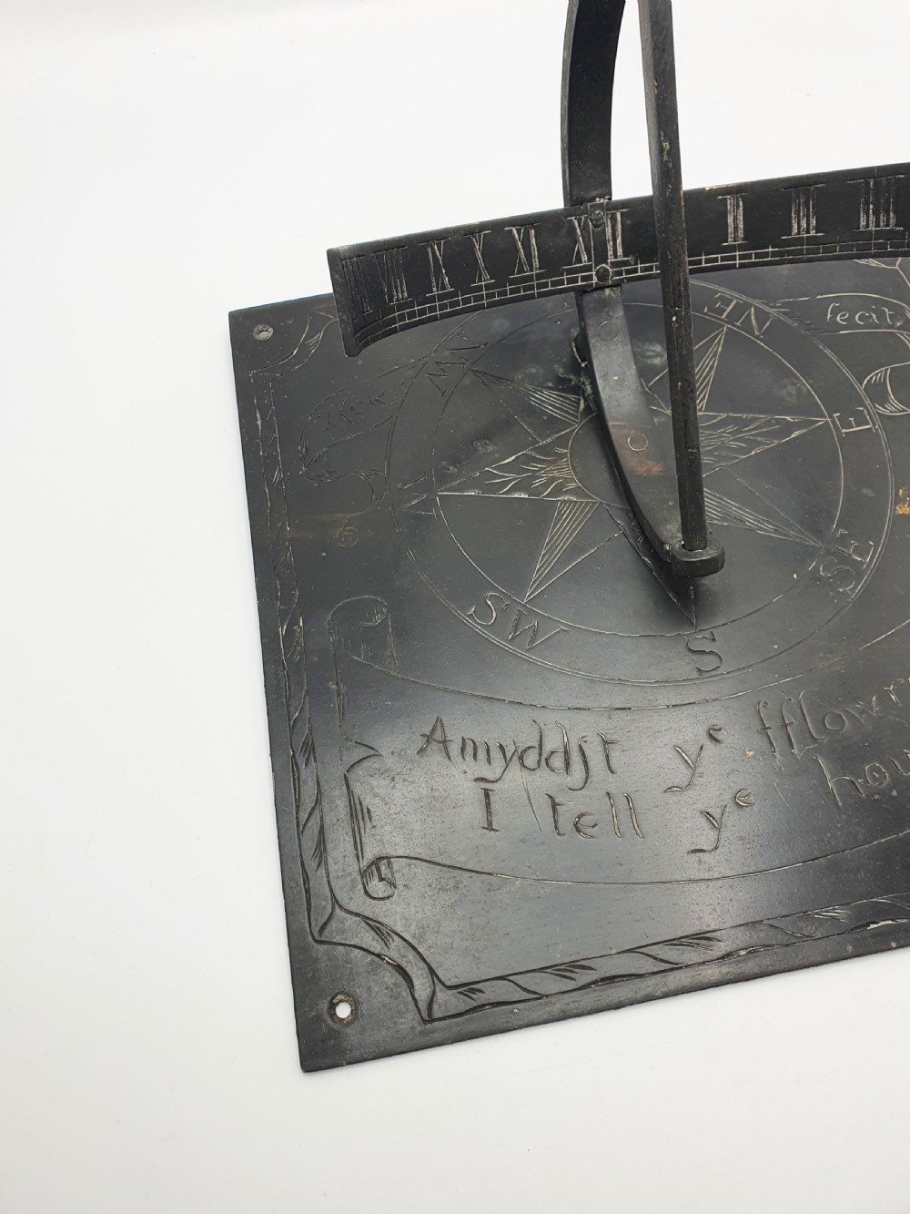 A square dark patinated brass sundial plate featuring engraved compass markings, verse inscription, and a curved armillary gnomon arc. View VI