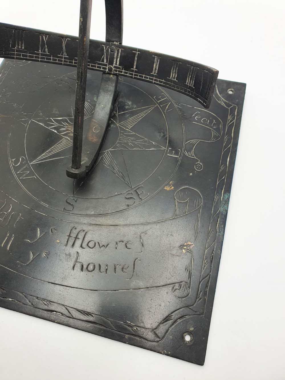 A square dark patinated brass sundial plate featuring engraved compass markings, verse inscription, and a curved armillary gnomon arc. View VII