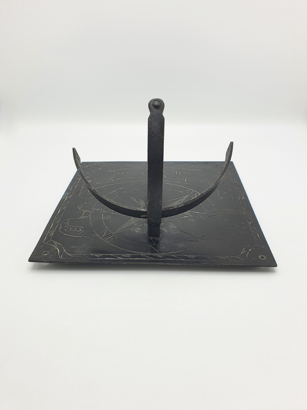 A square dark patinated brass sundial plate featuring engraved compass markings, verse inscription, and a curved armillary gnomon arc. View VIII