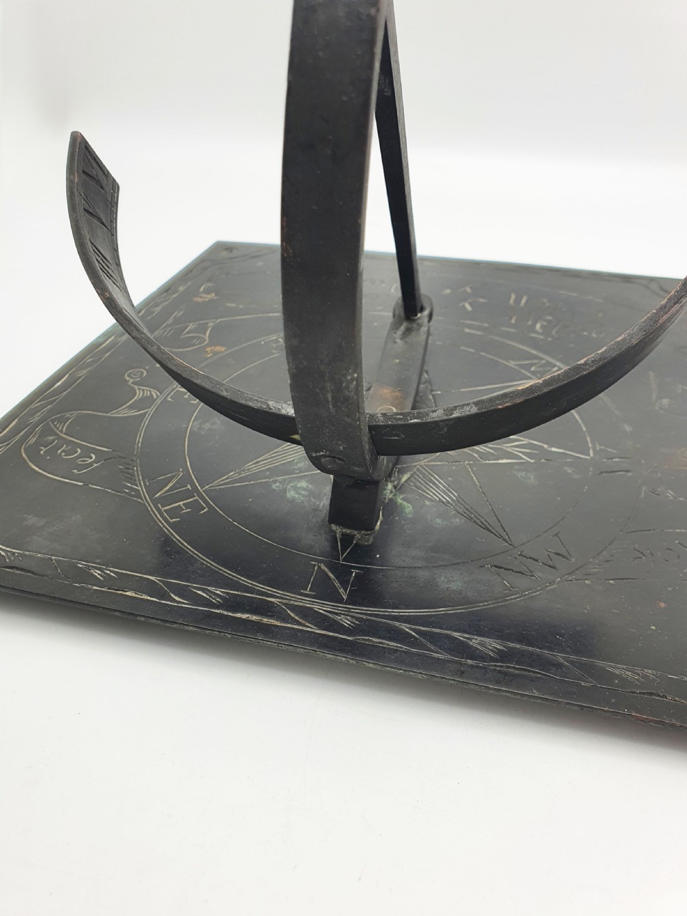 A square dark patinated brass sundial plate featuring engraved compass markings, verse inscription, and a curved armillary gnomon arc. View IX