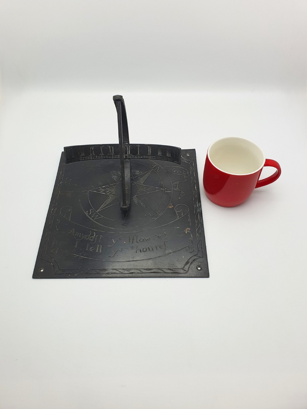 A square dark patinated brass sundial plate featuring engraved compass markings, verse inscription, and a curved armillary gnomon arc. View XI