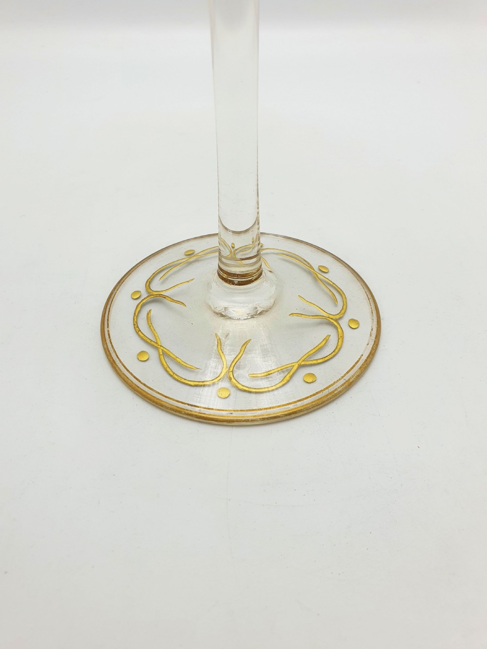 A clear glass tazza featuring a wide shallow bowl decorated with gilded grapevines, set on a tall slender stem and a circular gilded base. View VII