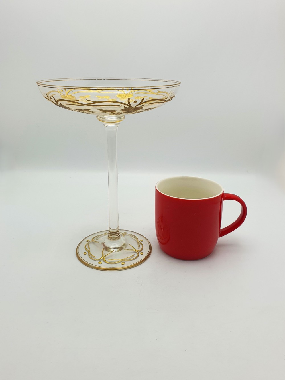 A clear glass tazza featuring a wide shallow bowl decorated with gilded grapevines, set on a tall slender stem and a circular gilded base. View VIII
