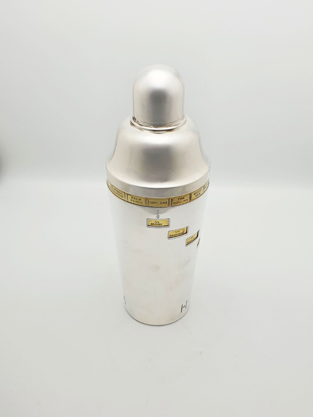 A vintage silver-plated cocktail shaker featuring a rotating outer body with cutout windows displaying drink ingredient recipes.