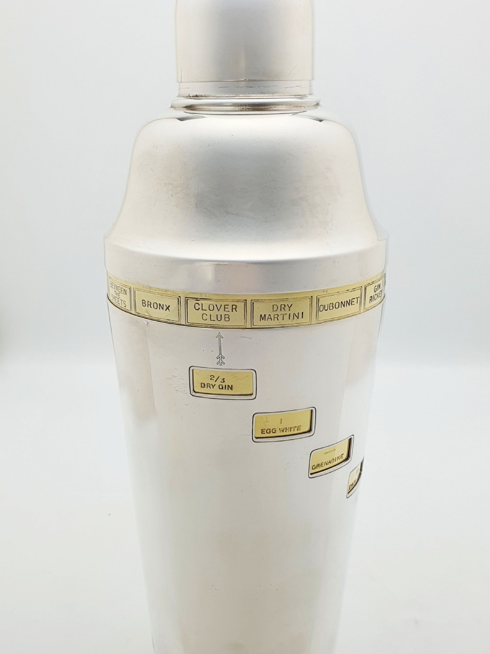 A vintage silver-plated cocktail shaker featuring a rotating outer body with cutout windows displaying drink ingredient recipes. View VI