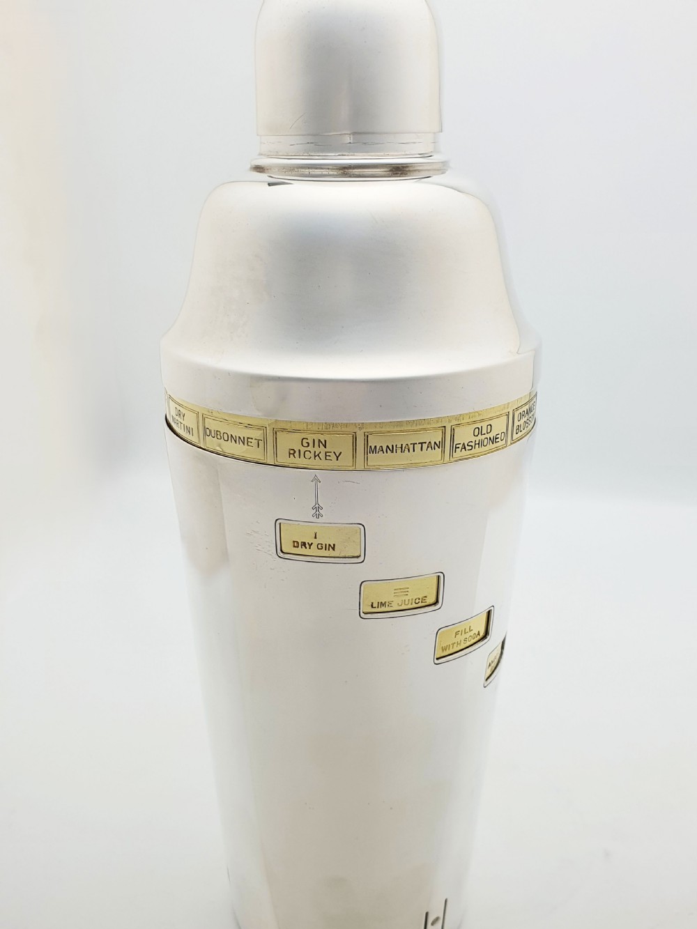 A vintage silver-plated cocktail shaker featuring a rotating outer body with cutout windows displaying drink ingredient recipes. View VII