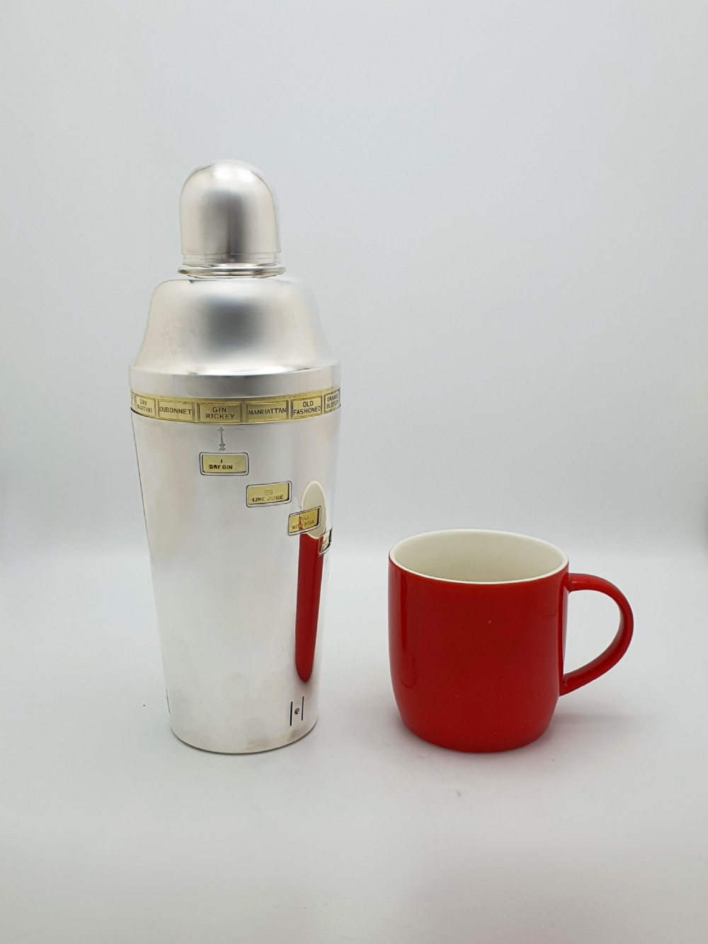 A vintage silver-plated cocktail shaker featuring a rotating outer body with cutout windows displaying drink ingredient recipes. View IX