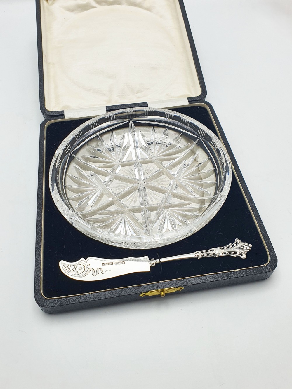 A circular cut crystal butter dish and a hallmarked sterling silver spreader presented inside a fitted black box.