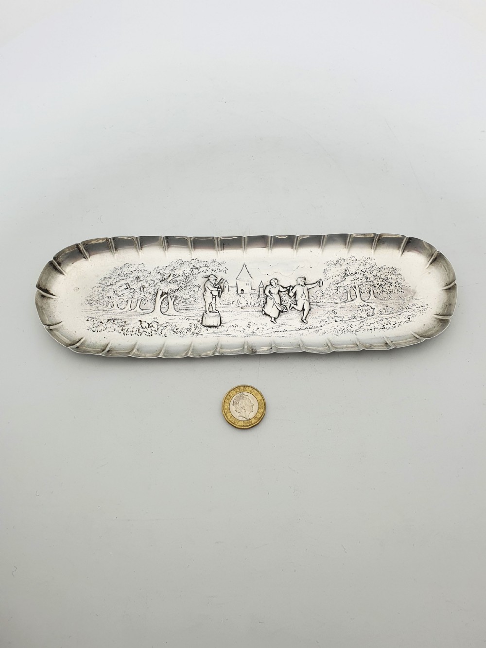 An elongated Victorian sterling silver tray featuring an embossed scene of a dancing couple and a musician surrounded by a fluted border. View VI