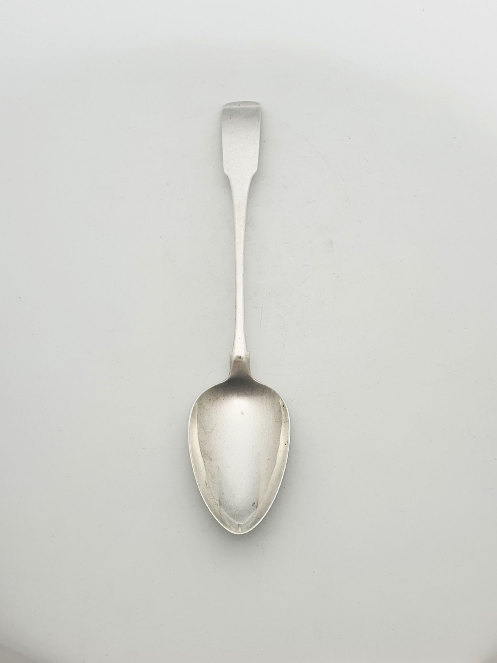 A Georgian sterling silver basting spoon featuring a long flat stem and oval bowl against a plain light background.