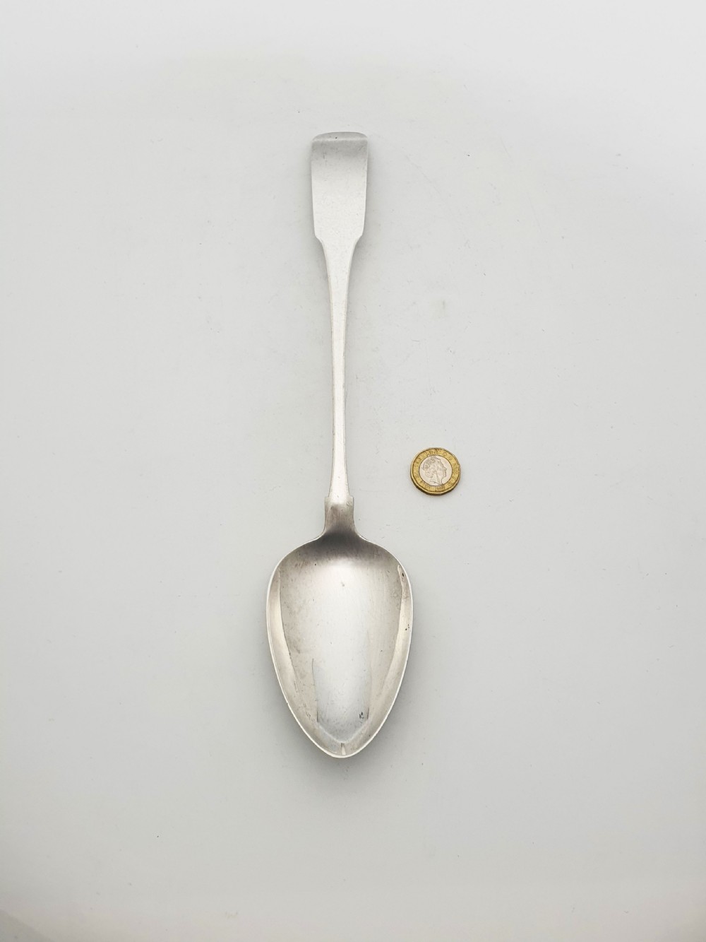 A Georgian sterling silver basting spoon featuring a long flat stem and oval bowl against a plain light background. View IV