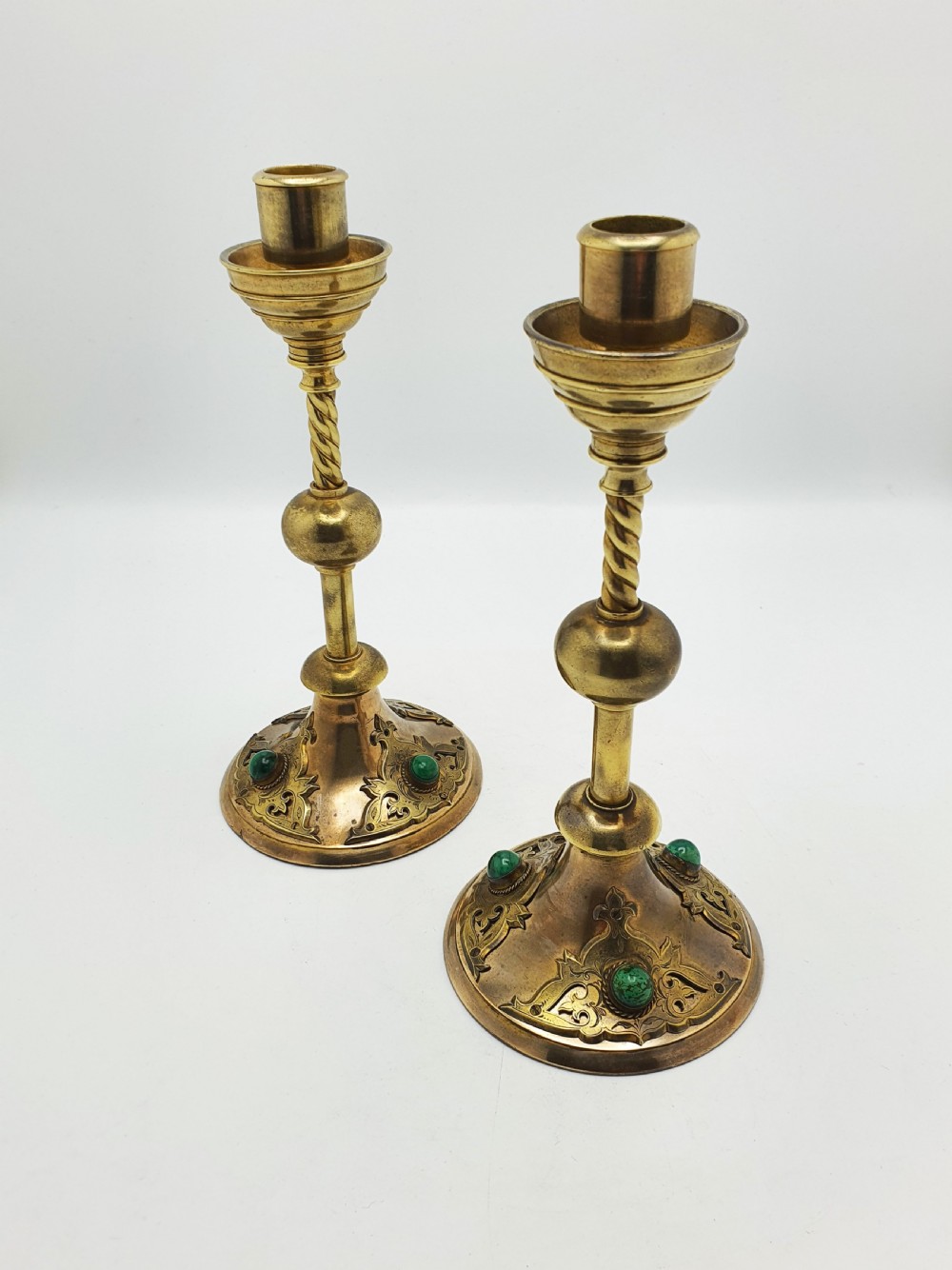 A pair of Victorian Gothic Revival brass candlesticks featuring spiral stems, spherical central knops, and circular bases with inset green cabochon stones.