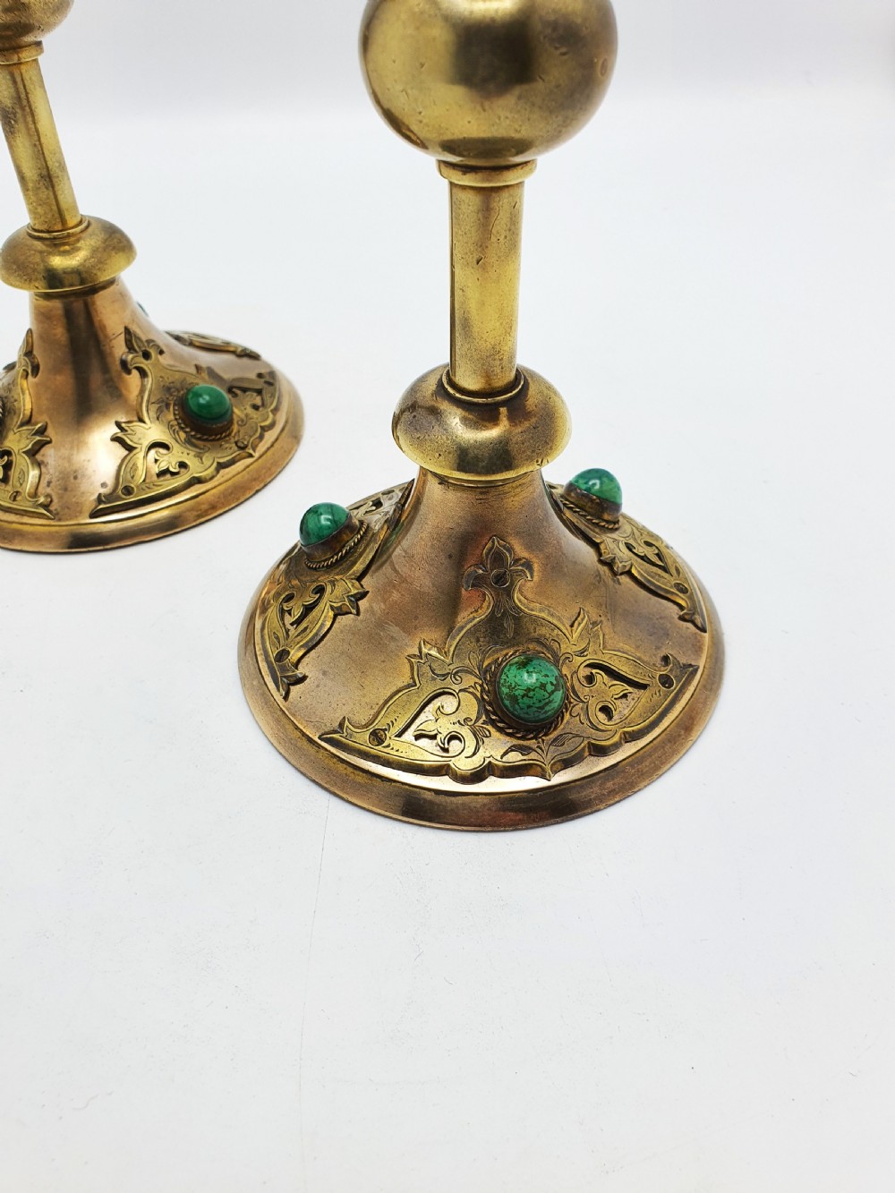 A pair of Victorian Gothic Revival brass candlesticks featuring spiral stems, spherical central knops, and circular bases with inset green cabochon stones. View II