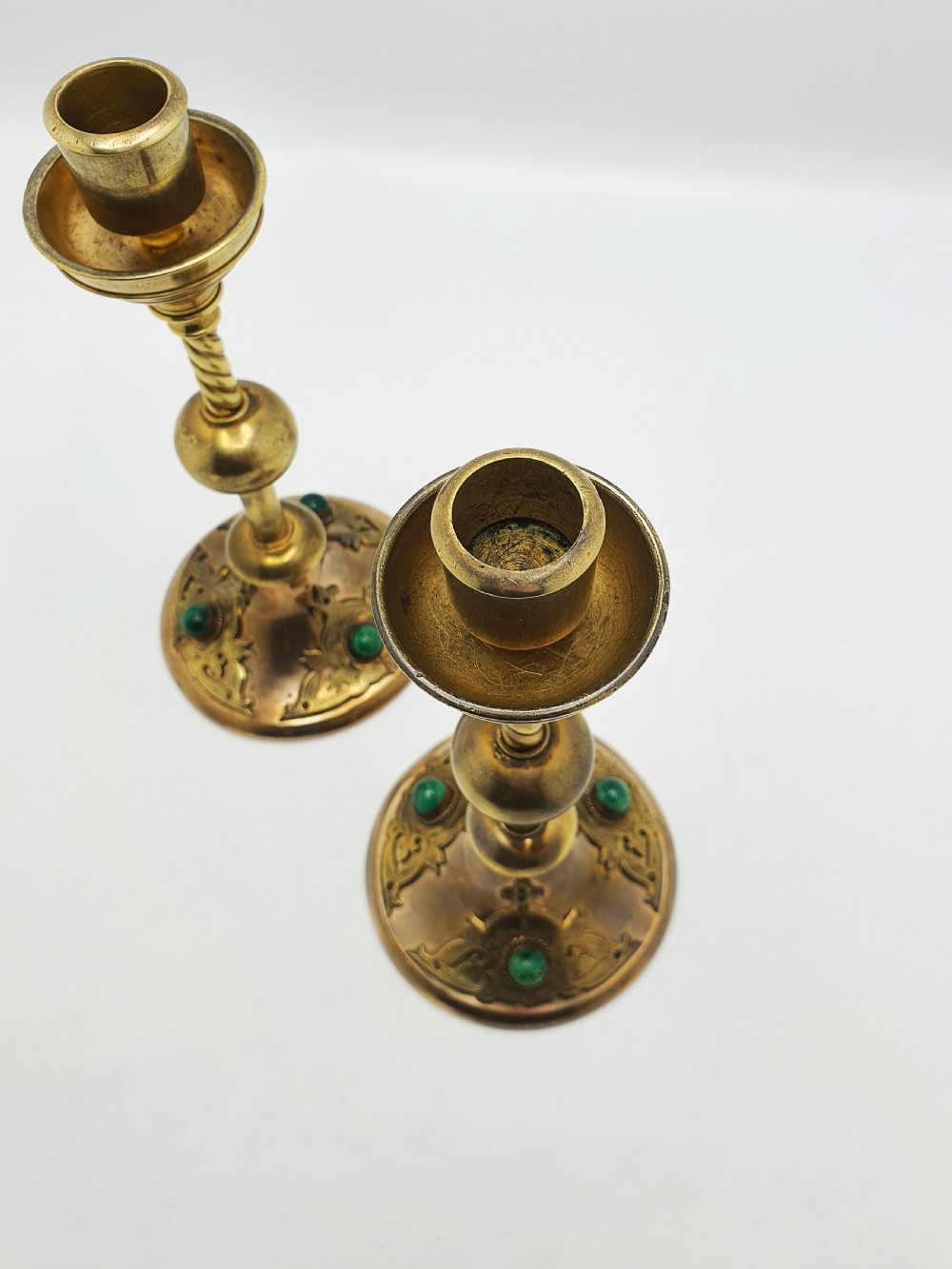 A pair of Victorian Gothic Revival brass candlesticks featuring spiral stems, spherical central knops, and circular bases with inset green cabochon stones. View V