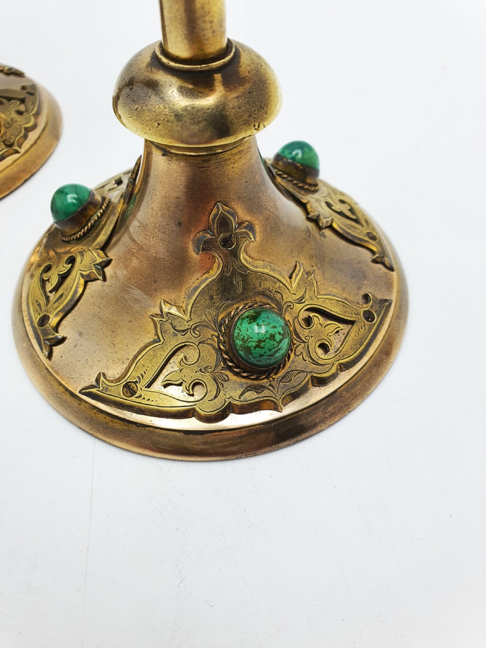 A pair of Victorian Gothic Revival brass candlesticks featuring spiral stems, spherical central knops, and circular bases with inset green cabochon stones. View VII