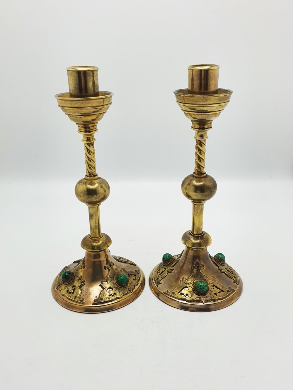 A pair of Victorian Gothic Revival brass candlesticks featuring spiral stems, spherical central knops, and circular bases with inset green cabochon stones. View VIII