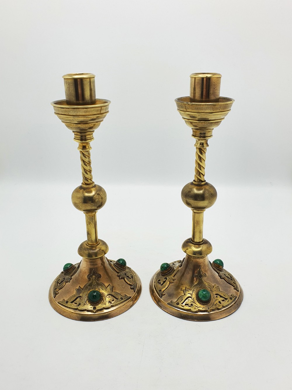 A pair of Victorian Gothic Revival brass candlesticks featuring spiral stems, spherical central knops, and circular bases with inset green cabochon stones. View IX