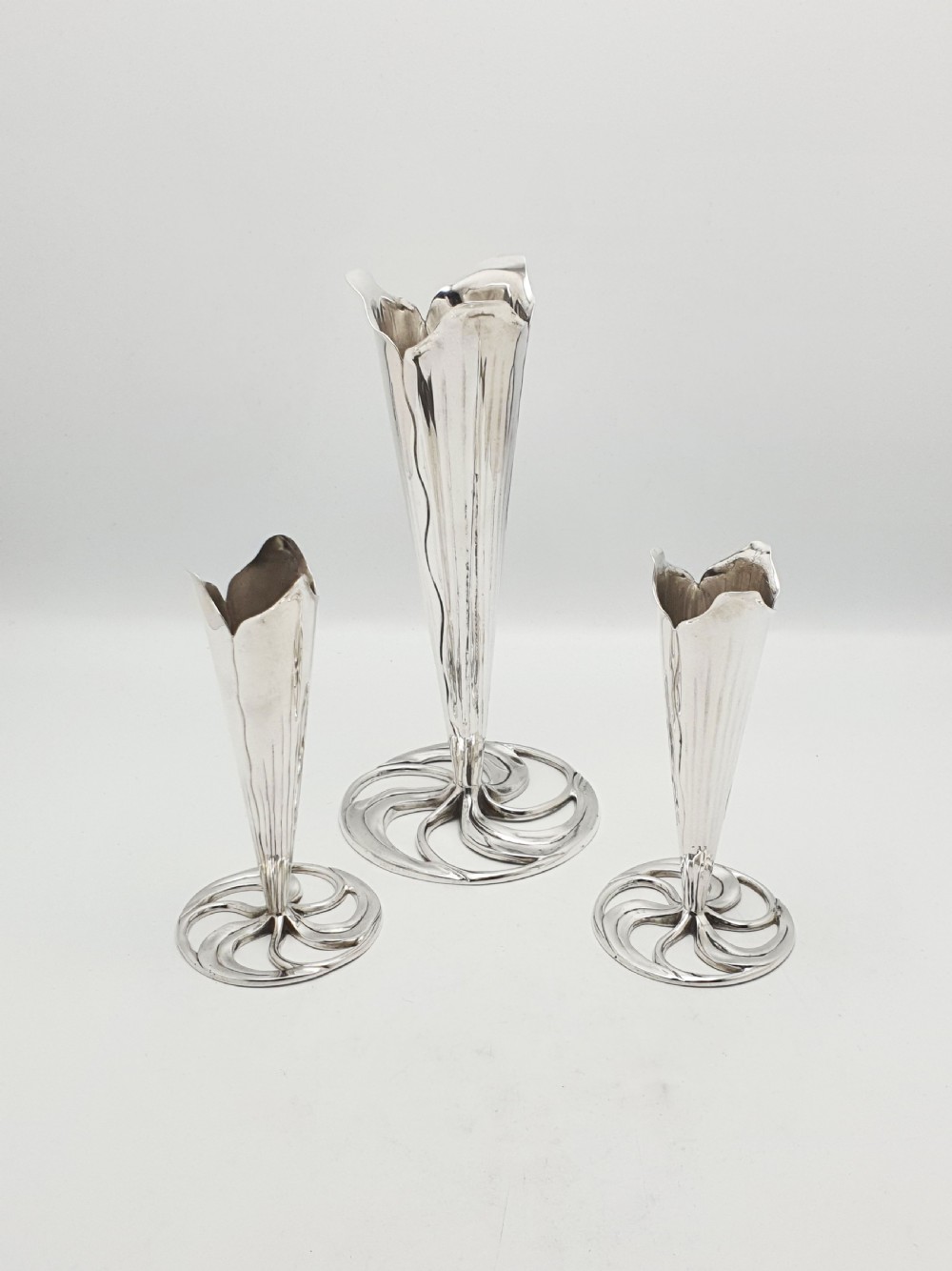 A set of three silver-plated trumpet vases with fluted rims and openwork swirl bases of varying heights.