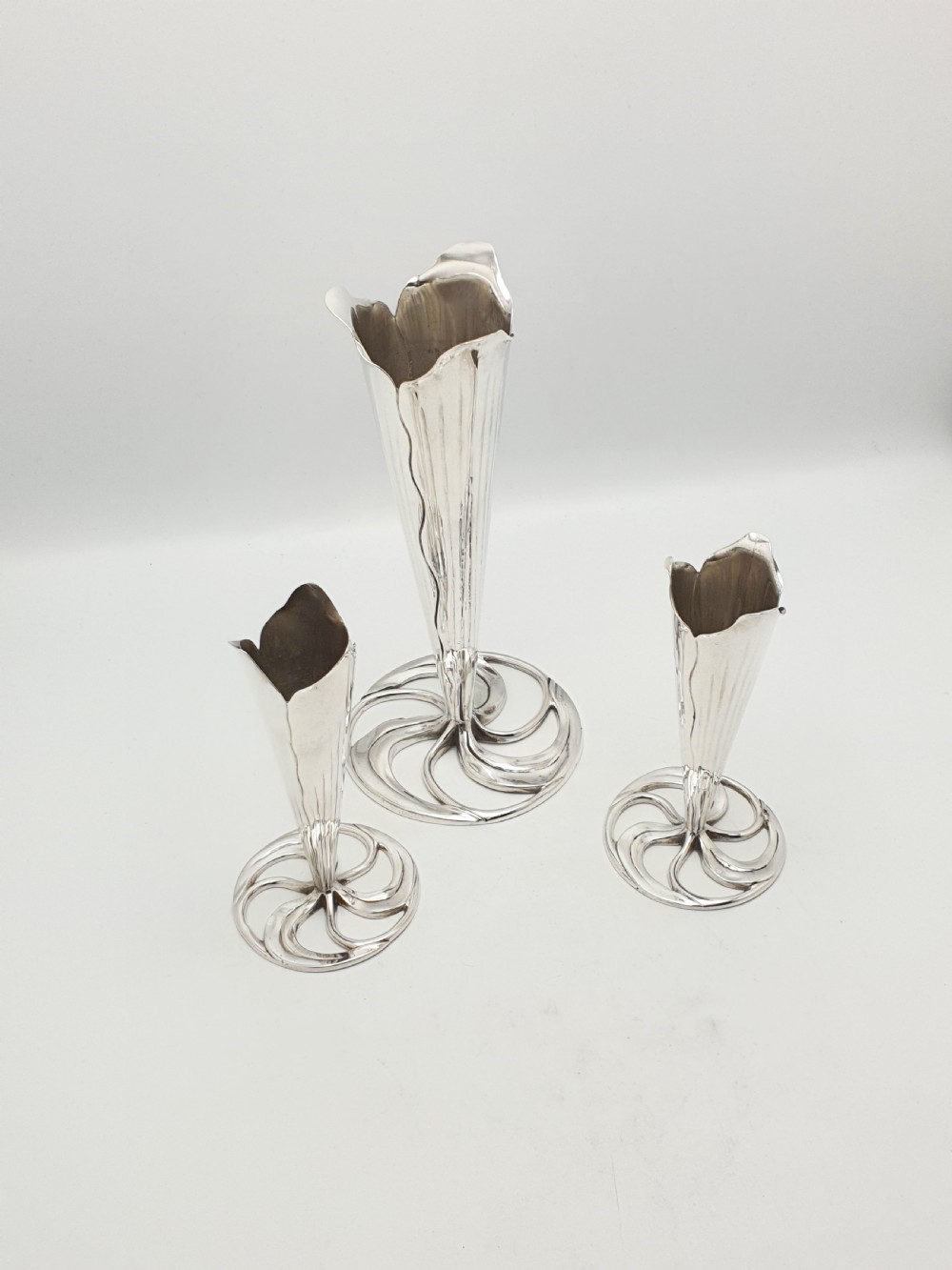 A set of three silver-plated trumpet vases with fluted rims and openwork swirl bases of varying heights. View II