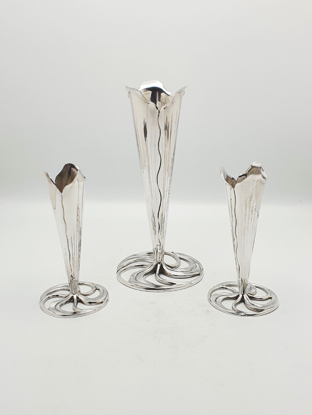 A set of three silver-plated trumpet vases with fluted rims and openwork swirl bases of varying heights. View V