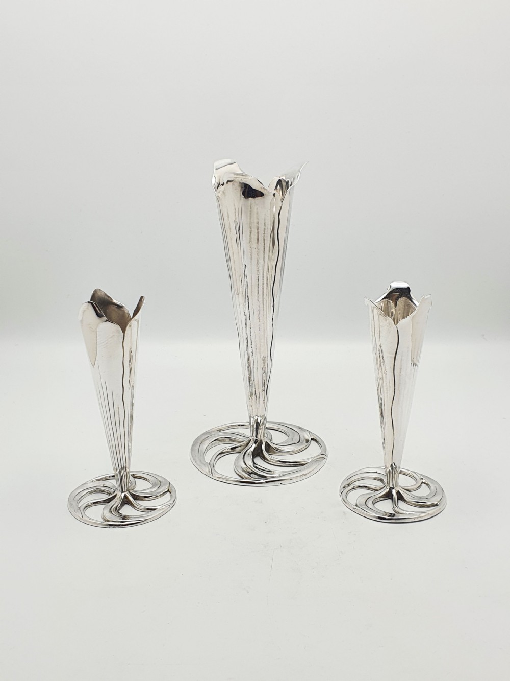 A set of three silver-plated trumpet vases with fluted rims and openwork swirl bases of varying heights. View VI