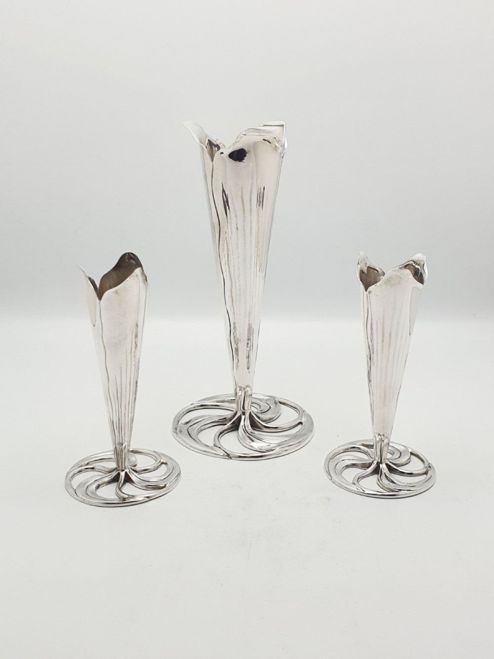 A set of three silver-plated trumpet vases with fluted rims and openwork swirl bases of varying heights. View VII