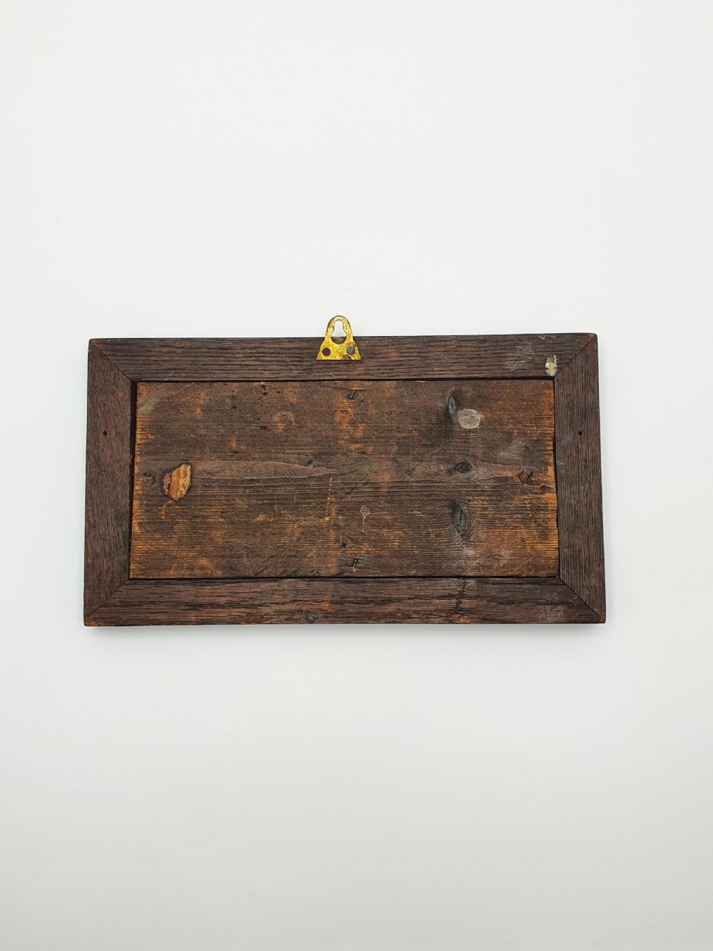 A rectangular copper relief plaque depicting an early steam locomotive and a large stone, mounted within a dark oak timber frame. View VI