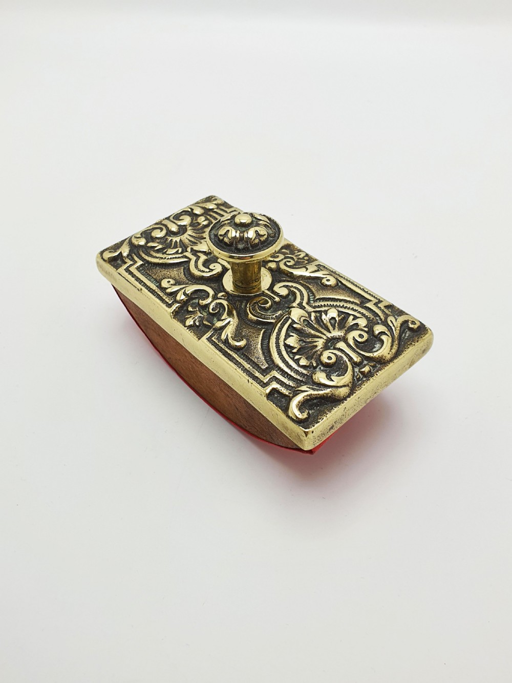 An Edwardian brass and wood rocker ink blotter featuring an ornate cast brass top plate decorated with relief scrollwork and a central turned brass knob handle.