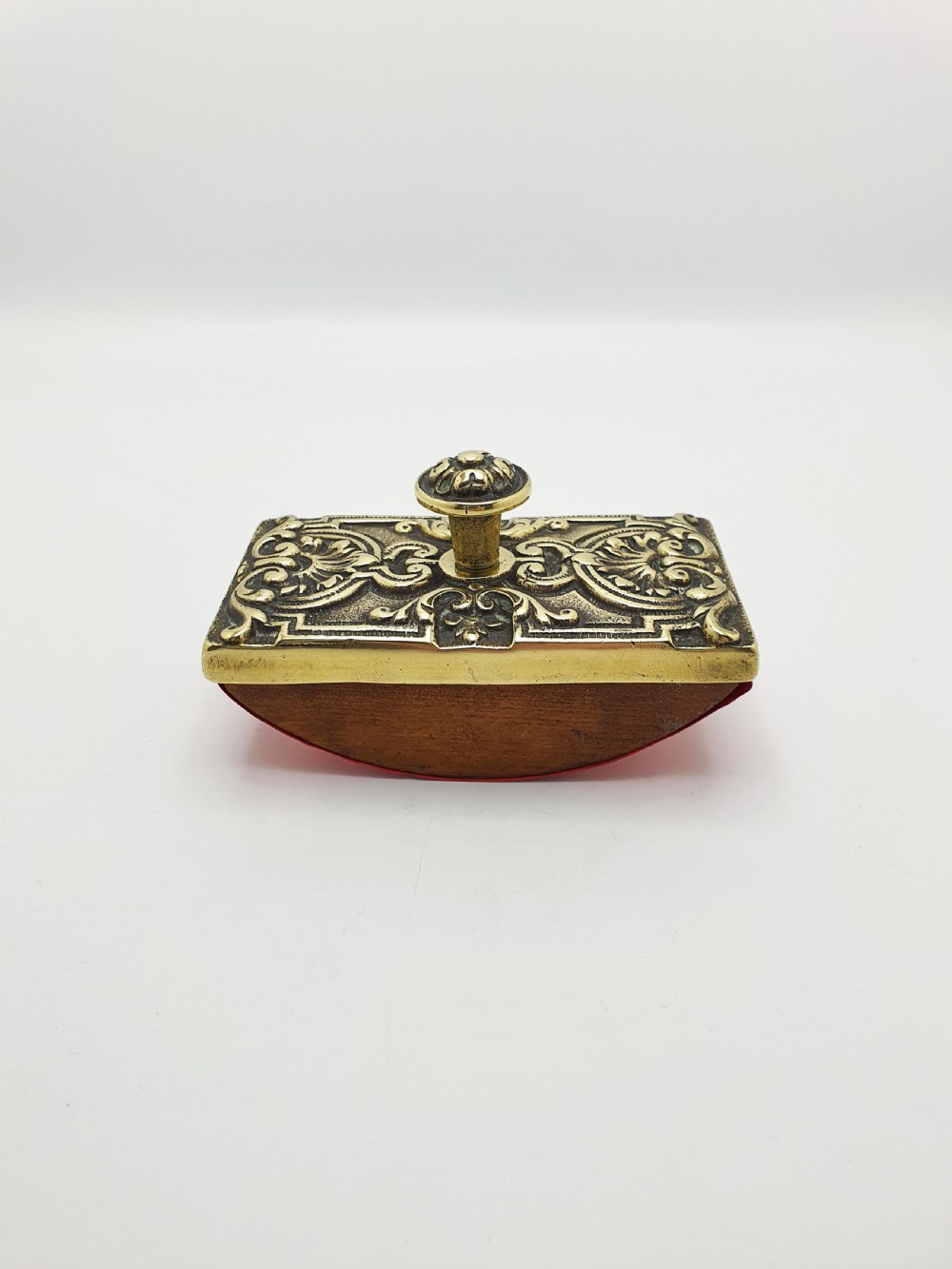 An Edwardian brass and wood rocker ink blotter featuring an ornate cast brass top plate decorated with relief scrollwork and a central turned brass knob handle. View II