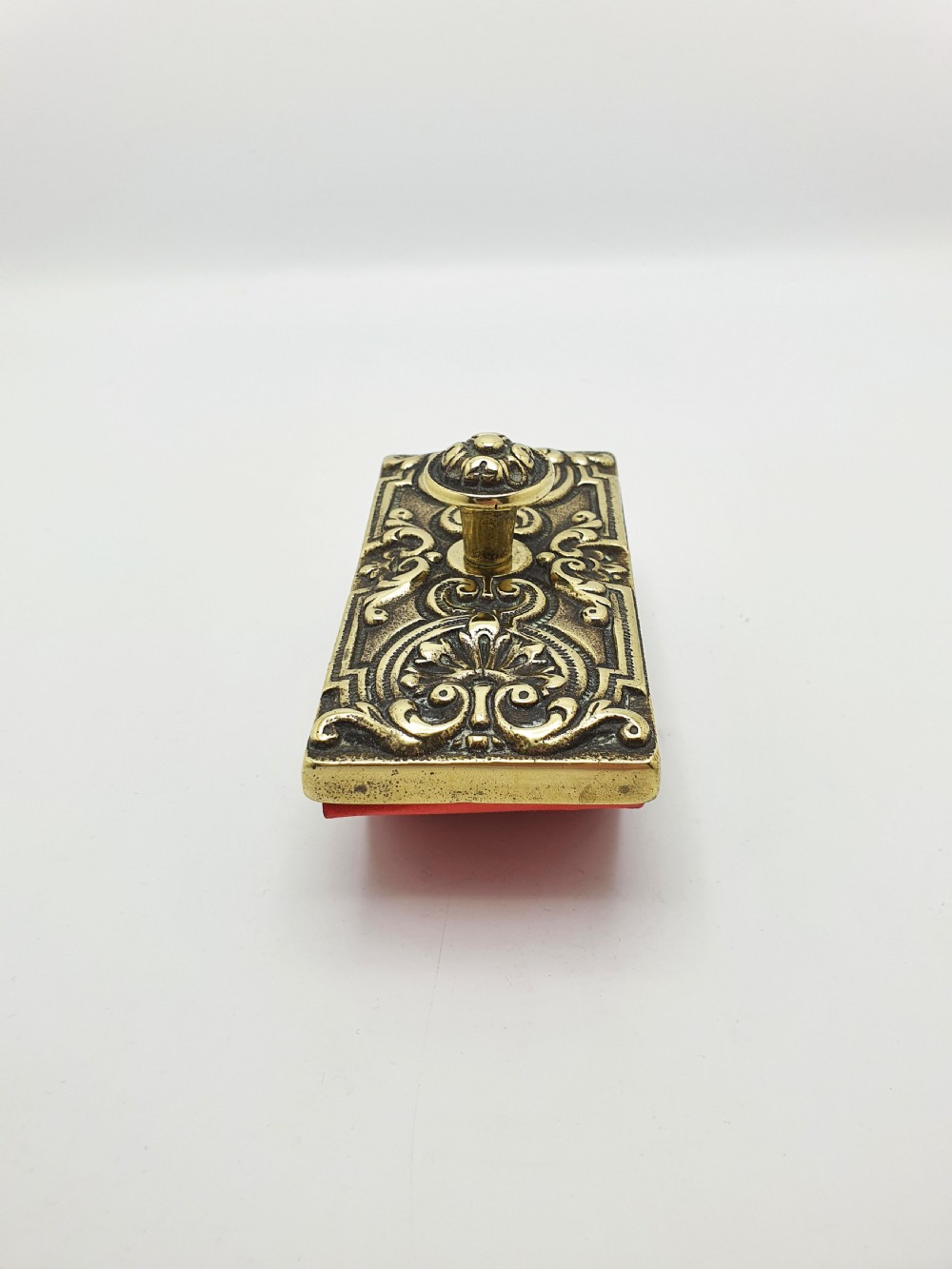 An Edwardian brass and wood rocker ink blotter featuring an ornate cast brass top plate decorated with relief scrollwork and a central turned brass knob handle. View III