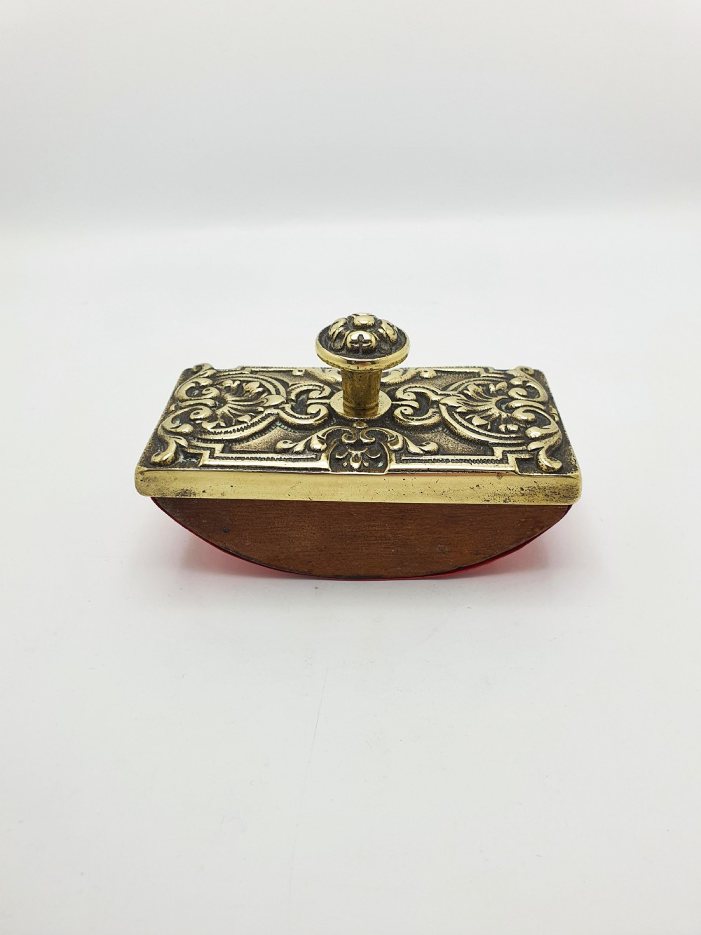 An Edwardian brass and wood rocker ink blotter featuring an ornate cast brass top plate decorated with relief scrollwork and a central turned brass knob handle. View V