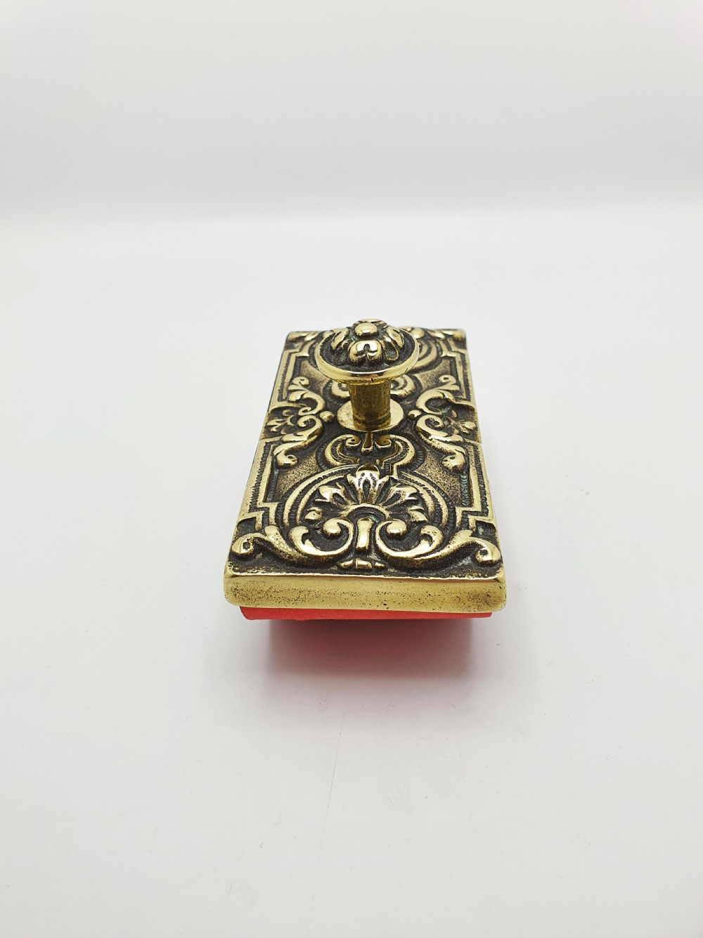 An Edwardian brass and wood rocker ink blotter featuring an ornate cast brass top plate decorated with relief scrollwork and a central turned brass knob handle. View VI