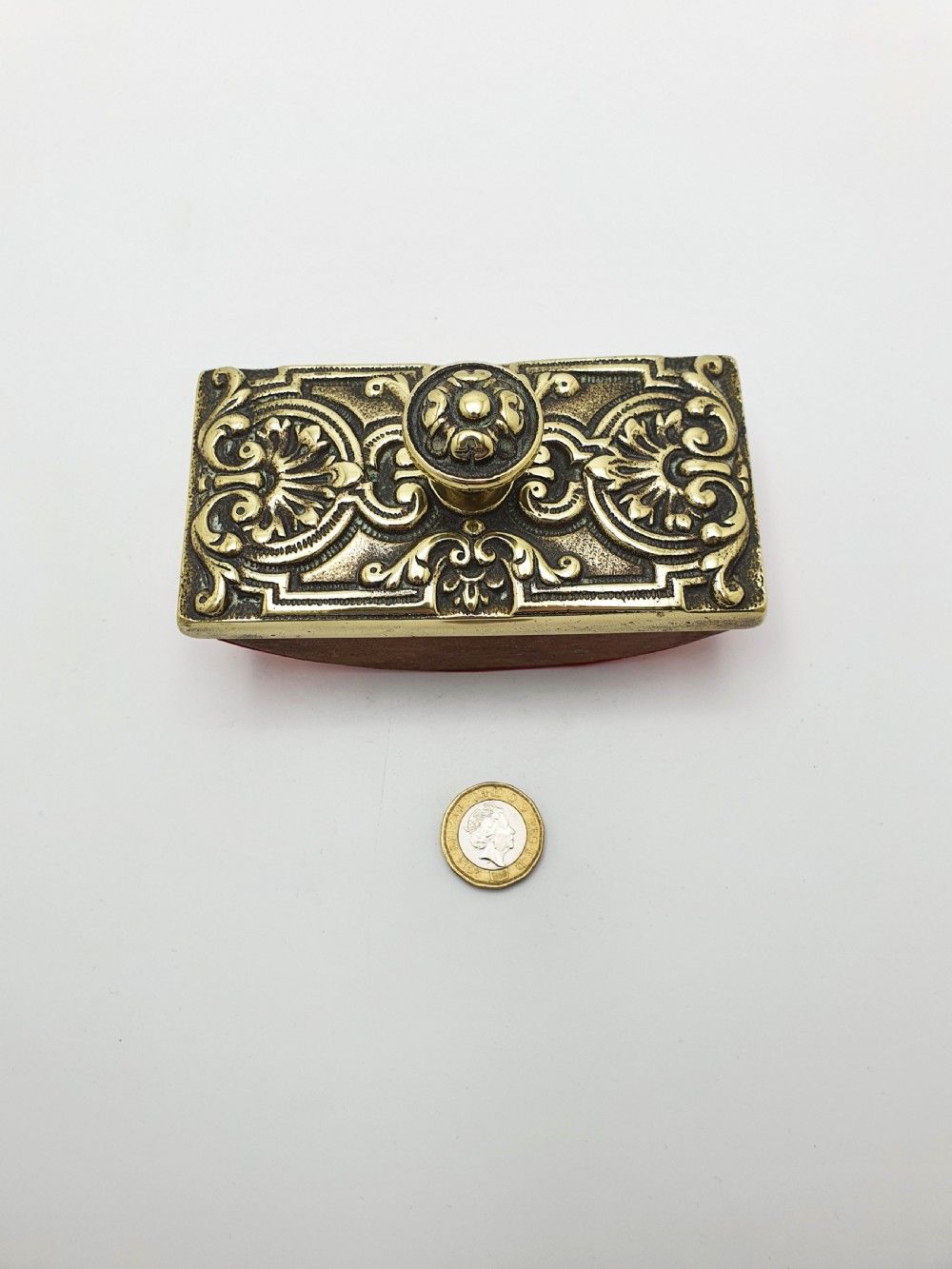 An Edwardian brass and wood rocker ink blotter featuring an ornate cast brass top plate decorated with relief scrollwork and a central turned brass knob handle. View IX
