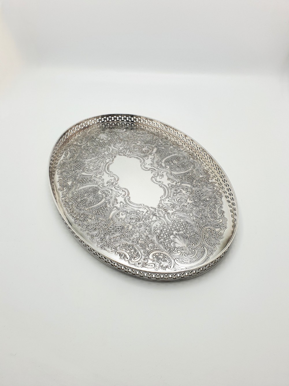 An oval silver-plated serving tray featuring a pierced gallery rim and an engraved surface with scroll motifs around a plain central cartouche.