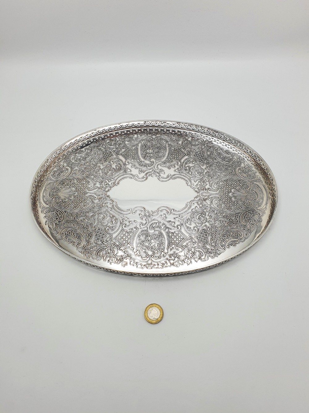 An oval silver-plated serving tray featuring a pierced gallery rim and an engraved surface with scroll motifs around a plain central cartouche. View VI