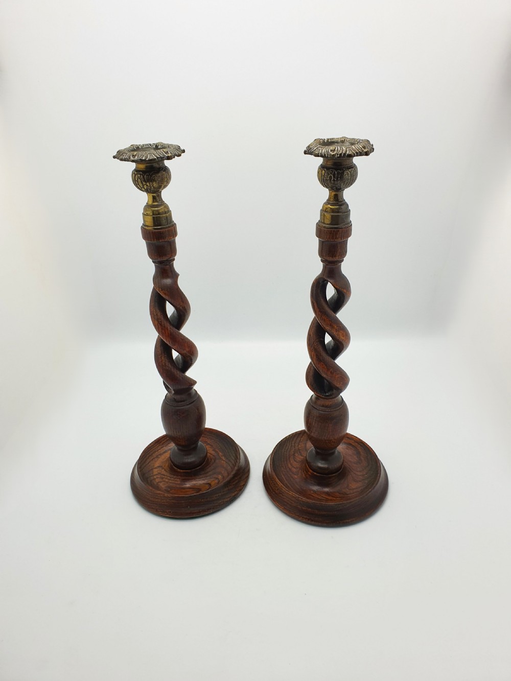 A pair of dark oak candlesticks featuring open barley twist shafts, circular stepped bases, and metal brass sconces. View II