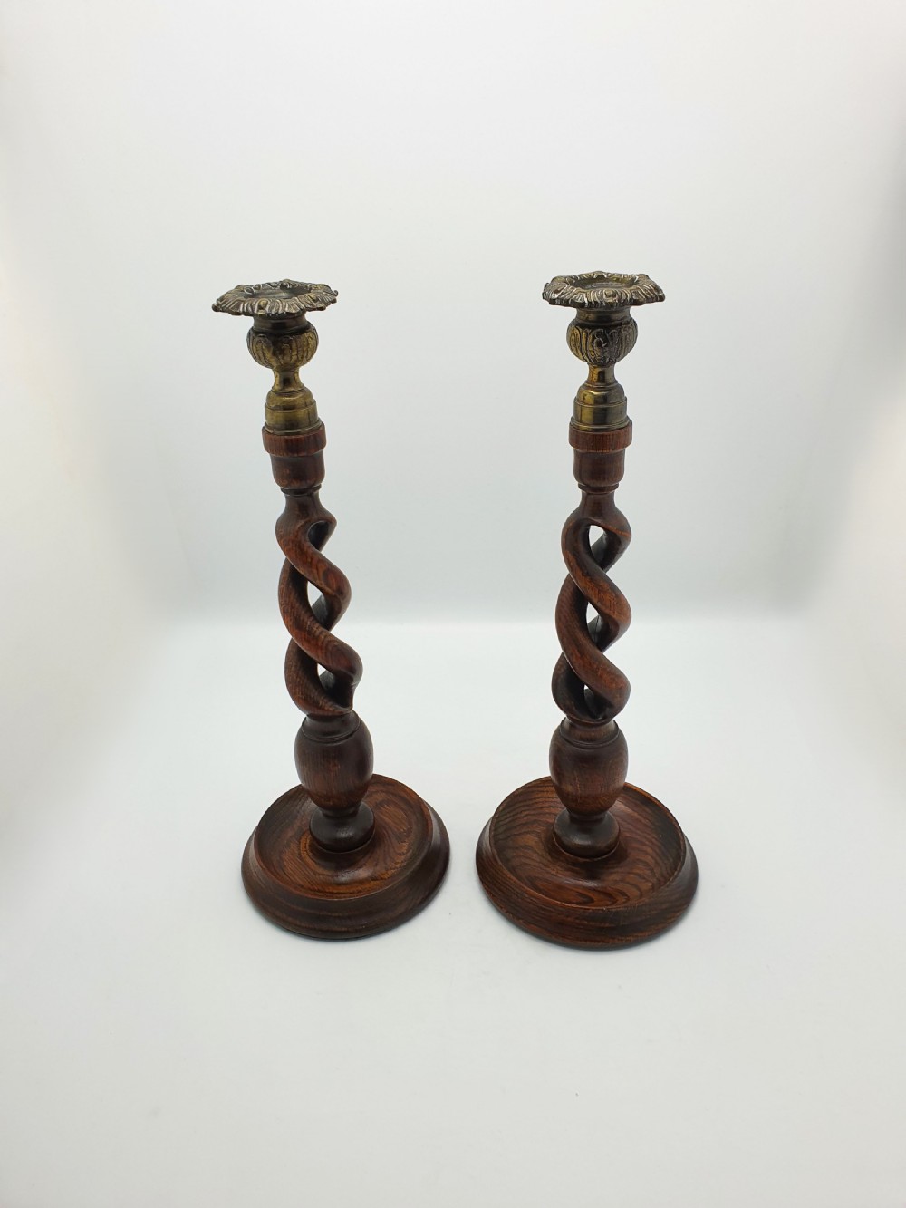 A pair of dark oak candlesticks featuring open barley twist shafts, circular stepped bases, and metal brass sconces. View III