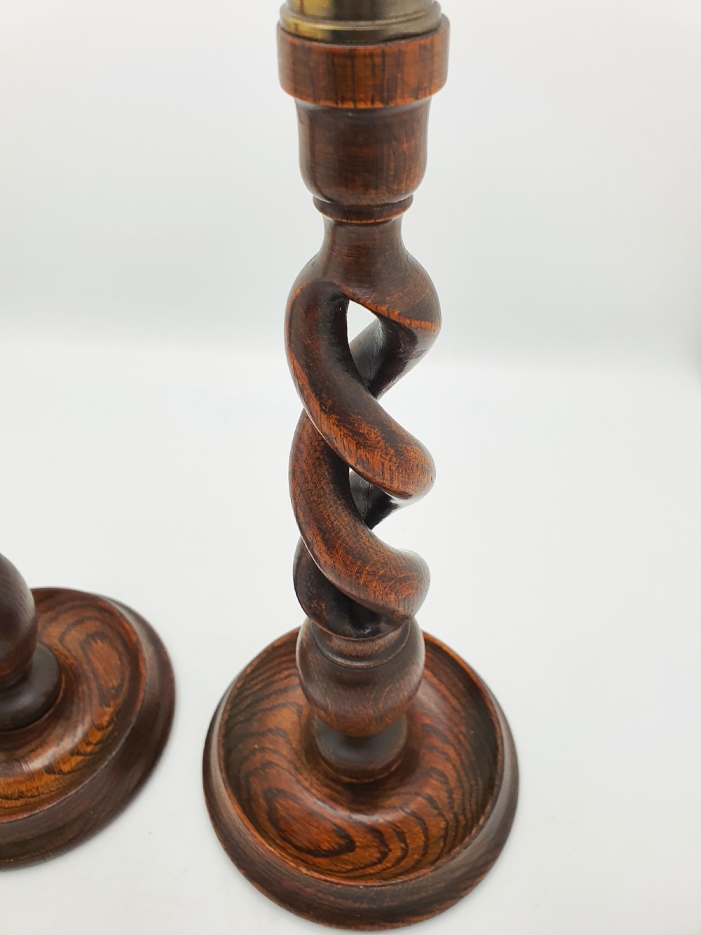 A pair of dark oak candlesticks featuring open barley twist shafts, circular stepped bases, and metal brass sconces. View V