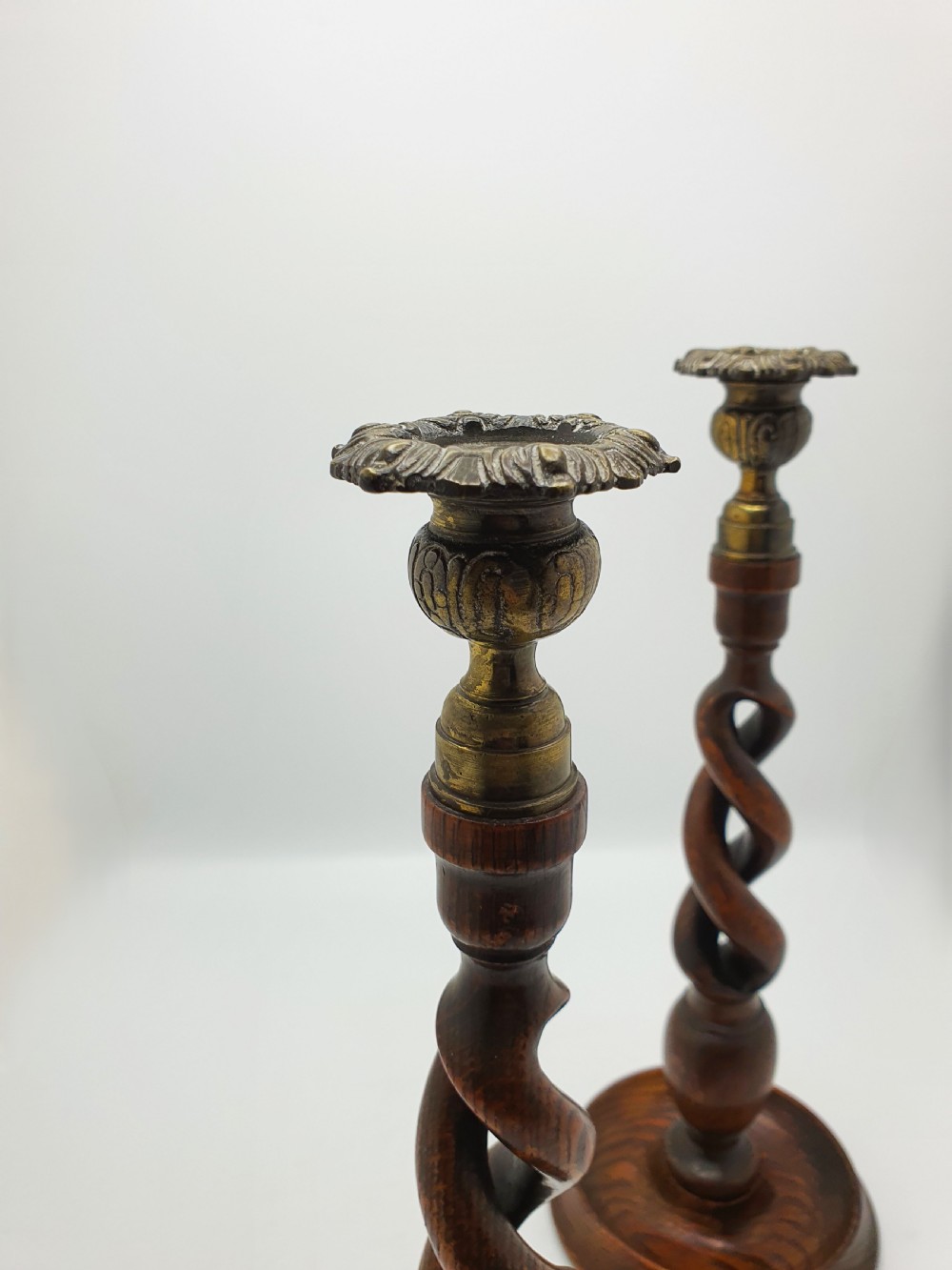 A pair of dark oak candlesticks featuring open barley twist shafts, circular stepped bases, and metal brass sconces. View IX