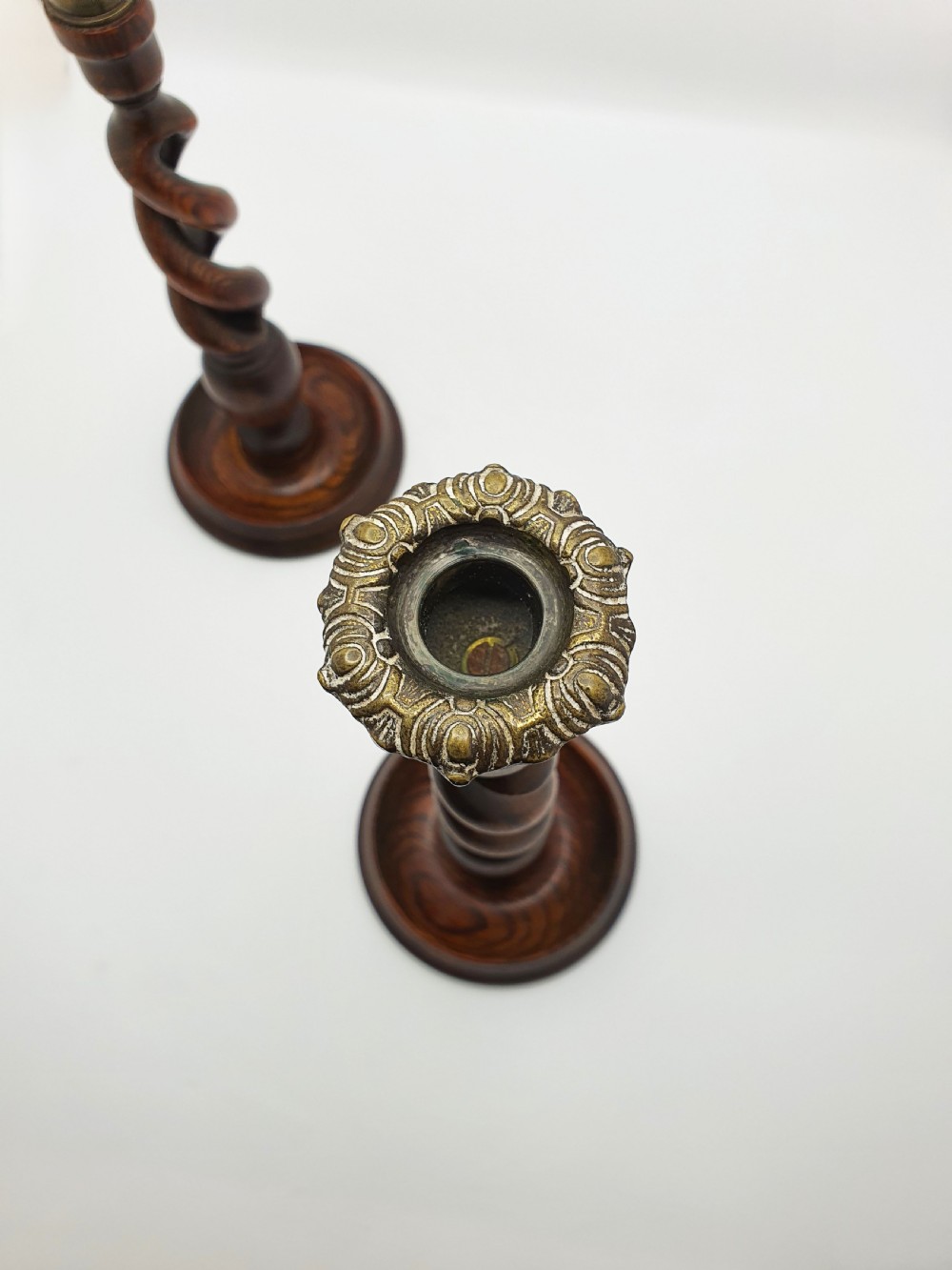 A pair of dark oak candlesticks featuring open barley twist shafts, circular stepped bases, and metal brass sconces. View X