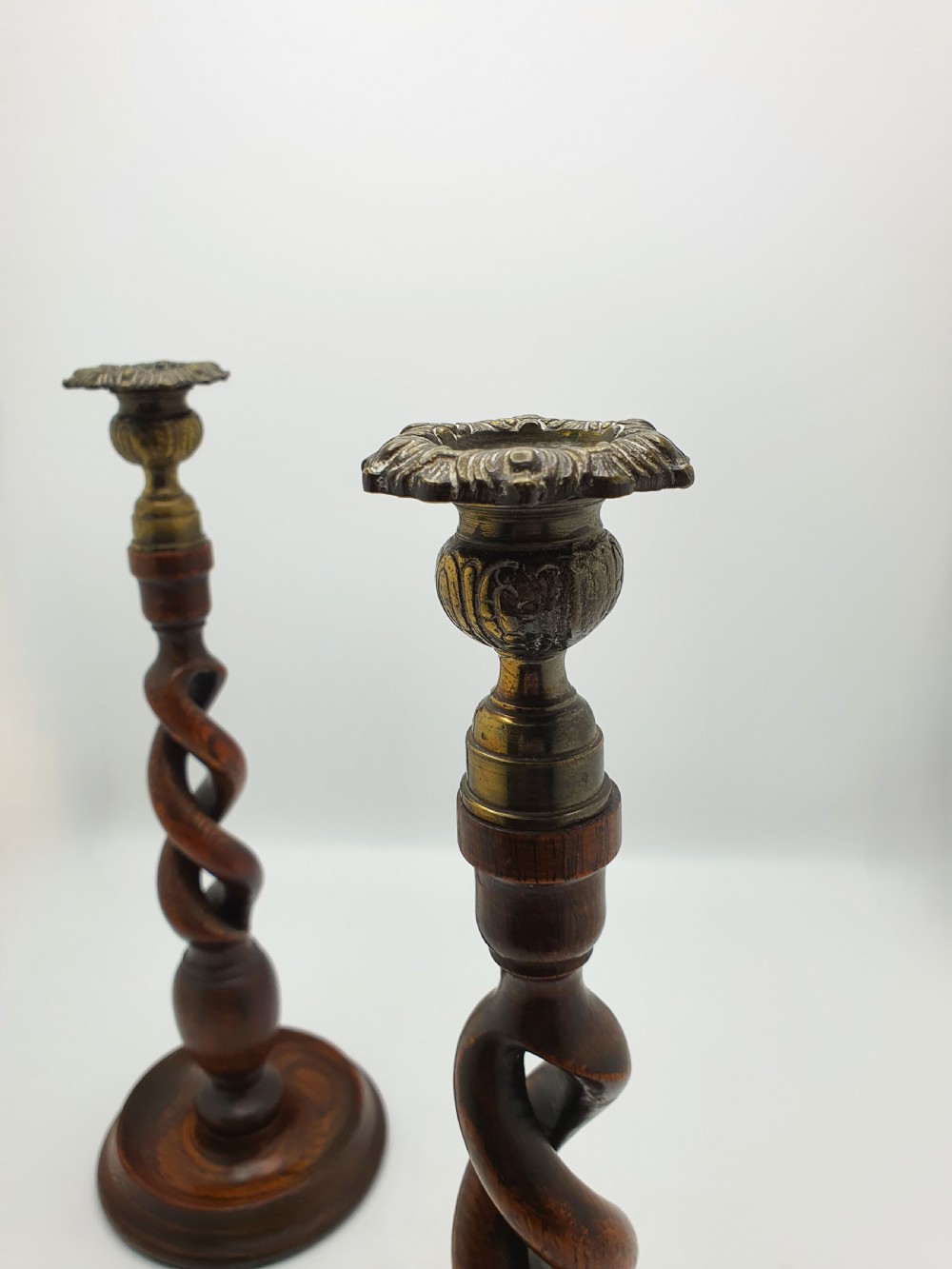 A pair of dark oak candlesticks featuring open barley twist shafts, circular stepped bases, and metal brass sconces. View XI