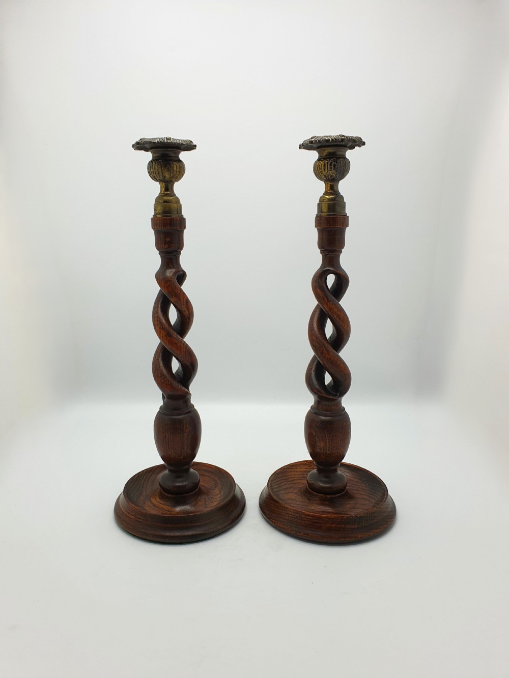 A pair of dark oak candlesticks featuring open barley twist shafts, circular stepped bases, and metal brass sconces. View XIV
