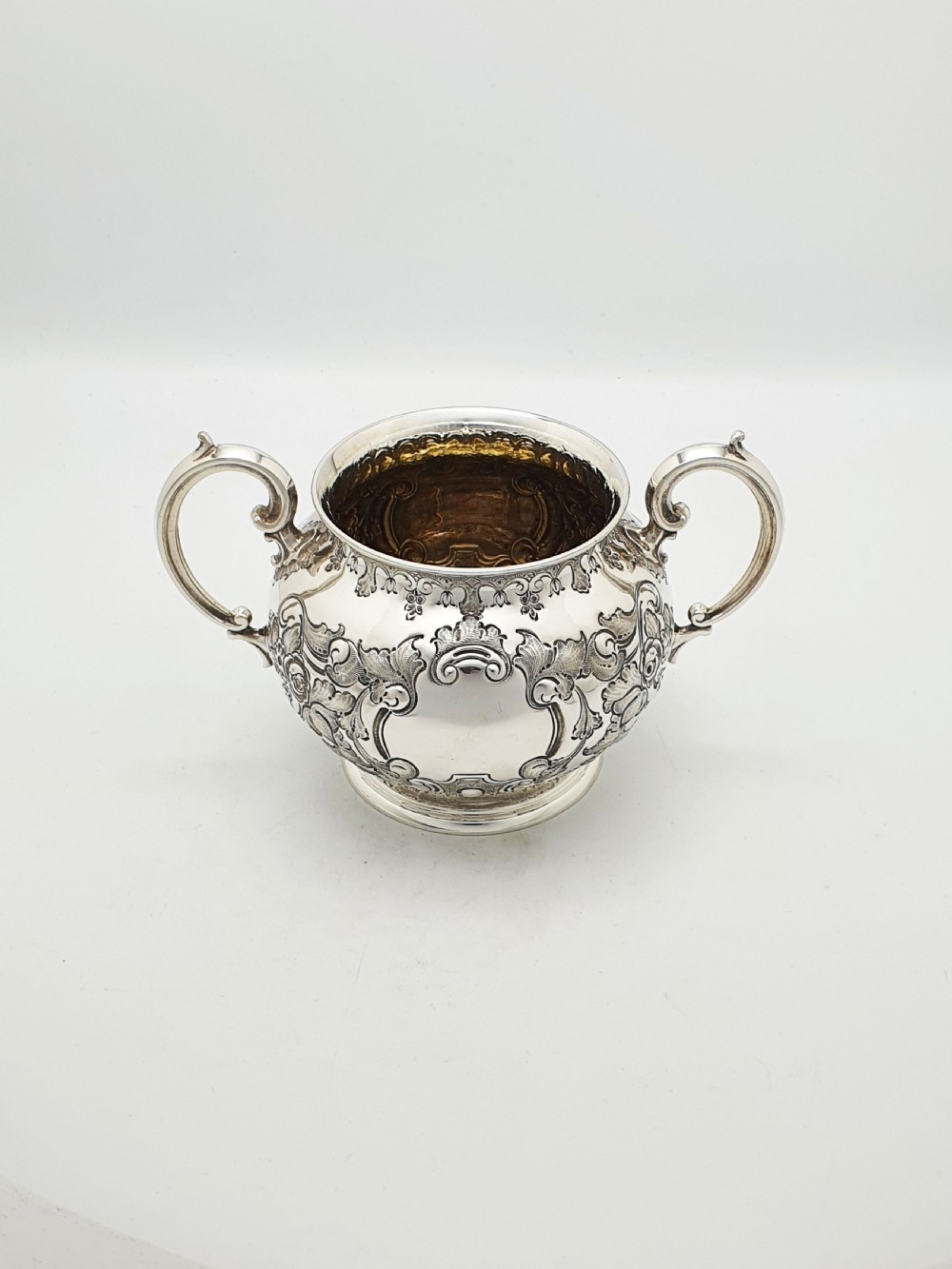 A two-piece Victorian silver-plated set featuring a milk jug and a double-handled sugar bowl, both decorated with intricate repousse floral scrollwork and lined with a gilded interior. View II