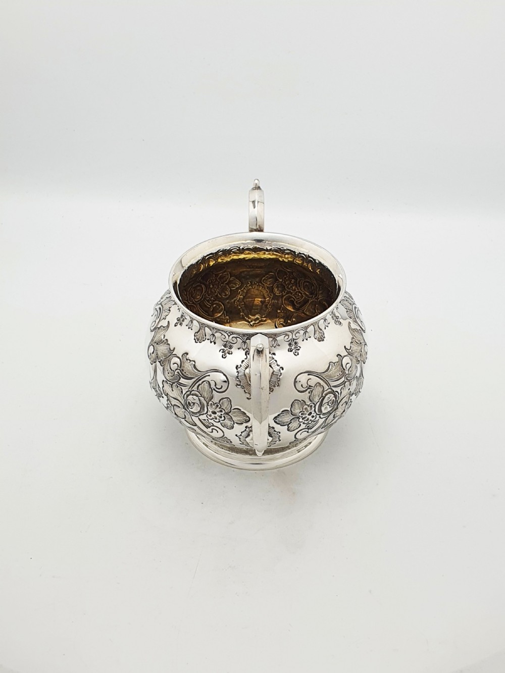 A two-piece Victorian silver-plated set featuring a milk jug and a double-handled sugar bowl, both decorated with intricate repousse floral scrollwork and lined with a gilded interior. View III