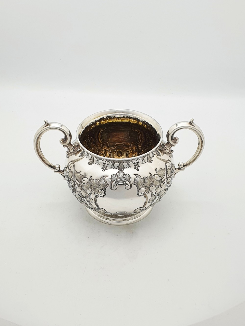 A two-piece Victorian silver-plated set featuring a milk jug and a double-handled sugar bowl, both decorated with intricate repousse floral scrollwork and lined with a gilded interior. View IV